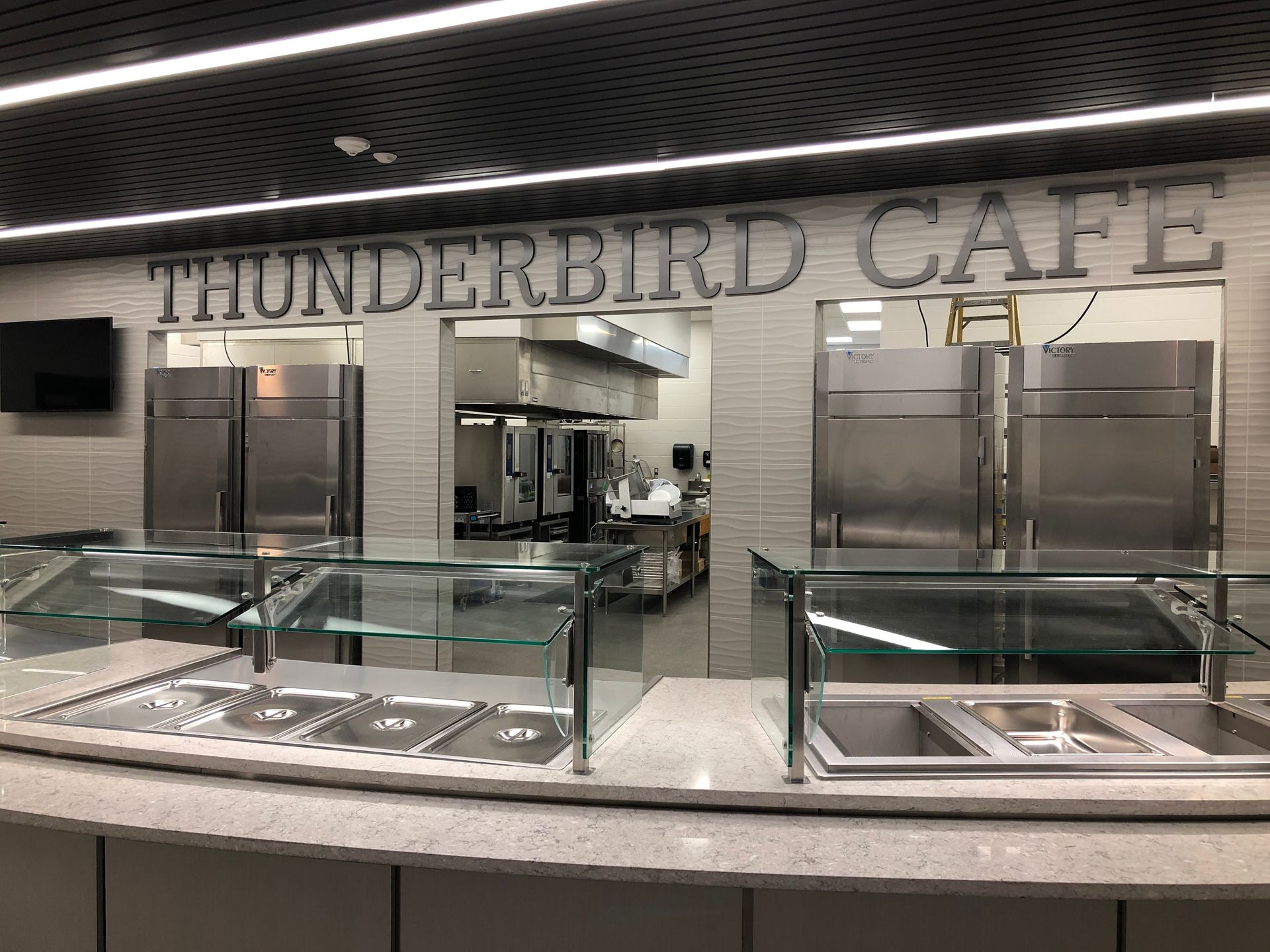 The Thunderbird Cafe featuring a food service counter with empty stainless steel trays and a view of a kitchen behind.