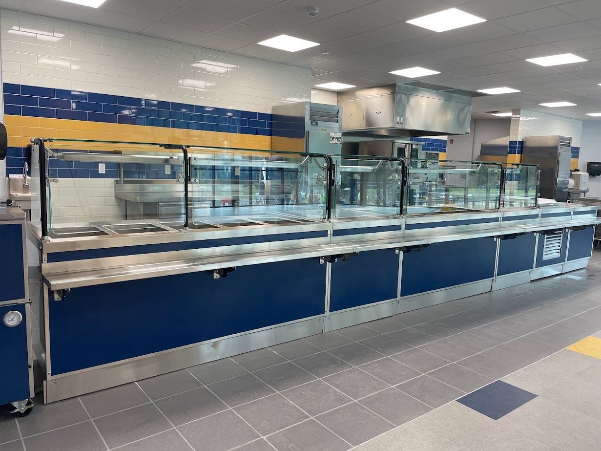 An empty cafeteria serving line with a long stainless steel counter, blue base panels, and glass food shields.