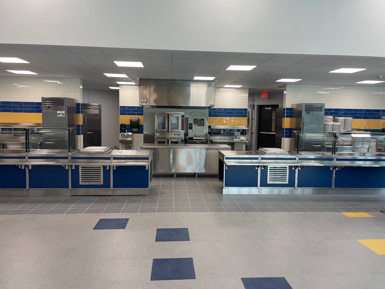A commercial kitchen serving area with stainless steel counters, blue cabinetry, and yellow wall accents.