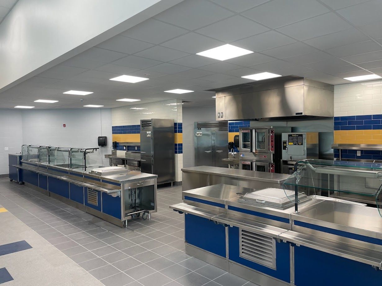 A commercial kitchen serving area with stainless steel counters, blue cabinetry, and overhead vent hoods.