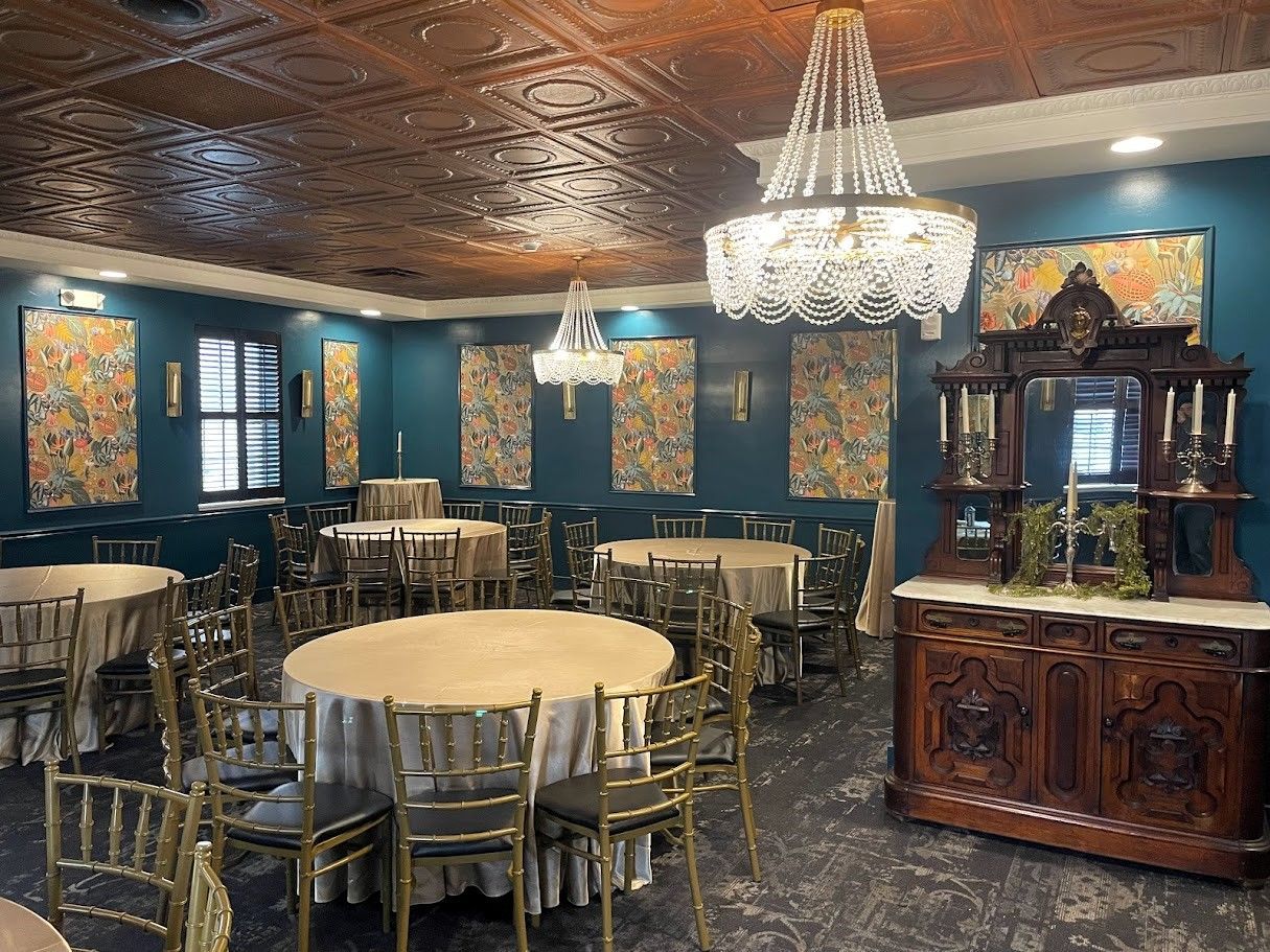 Elegant banquet room with round tables, gold chairs, teal walls, a dark copper ceiling, and a large crystal chandelier.