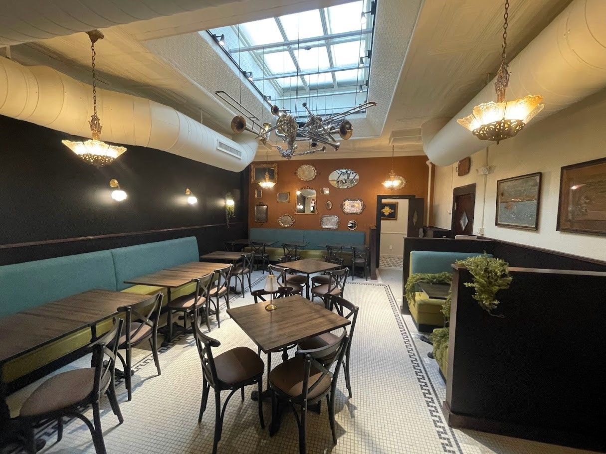 An interior view of a dining room with teal booths, wooden tables, chairs, and a glass ceiling skylight.