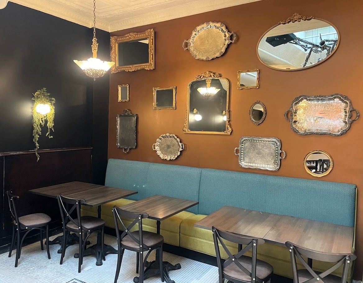 A cozy cafe corner with a teal booth, wooden tables, and an array of assorted decorative mirrors on a brown wall.