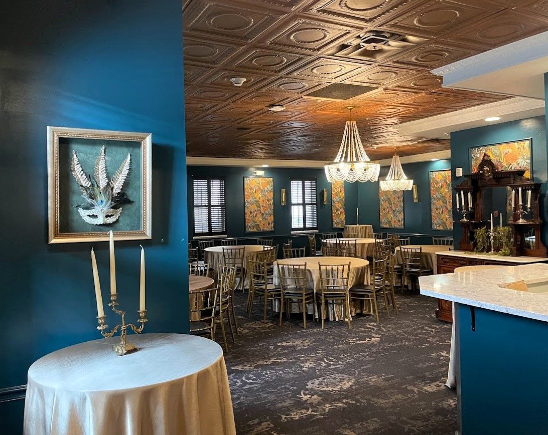 An elegant event space with teal walls, a copper-colored tin ceiling, chandelier lighting, and tables set for dining.