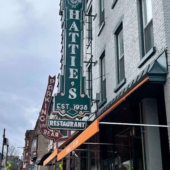 The iconic green vertical Hattie's Restaurant sign, established in 1938, hangs above an orange awning on a brick building.