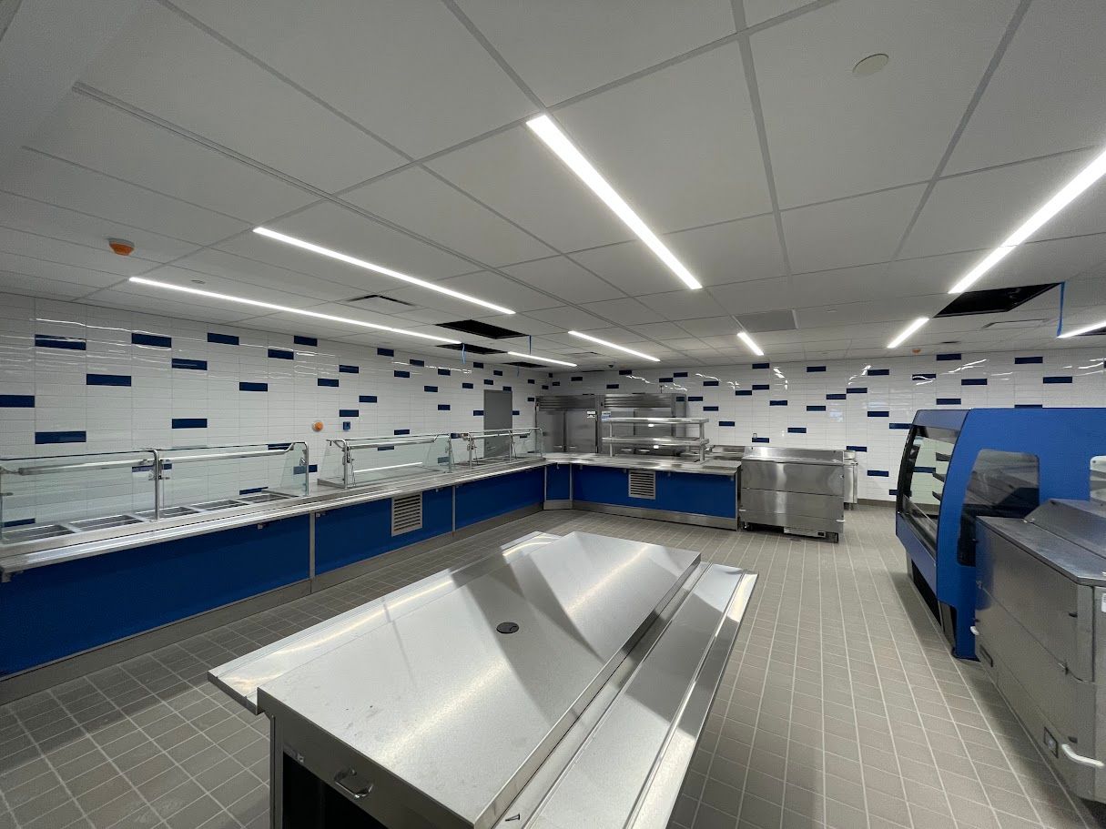 A modern school cafeteria service area with stainless steel counters, blue accents, and tiled walls and floors.