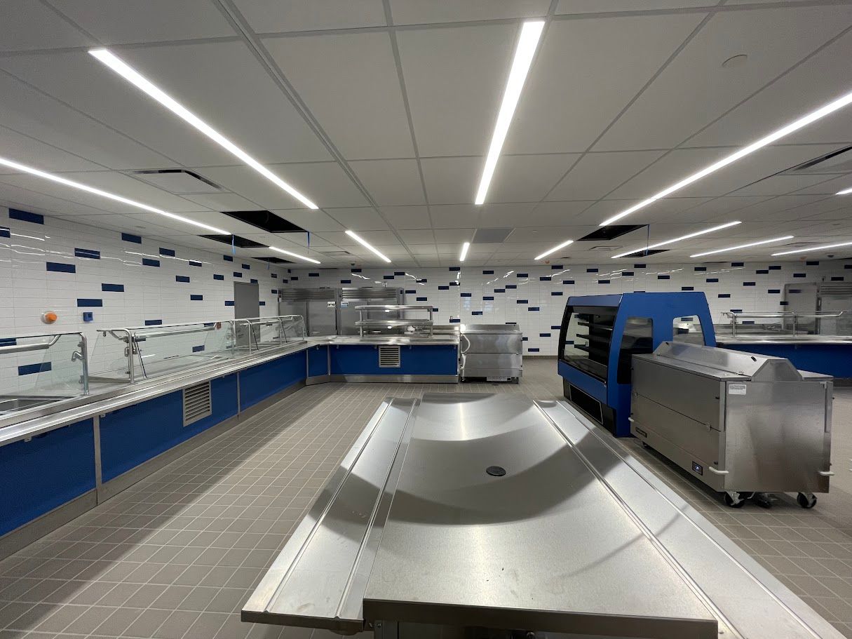 A wide view of a modern, empty school cafeteria serving area with stainless steel counters, blue trim, and tile walls.