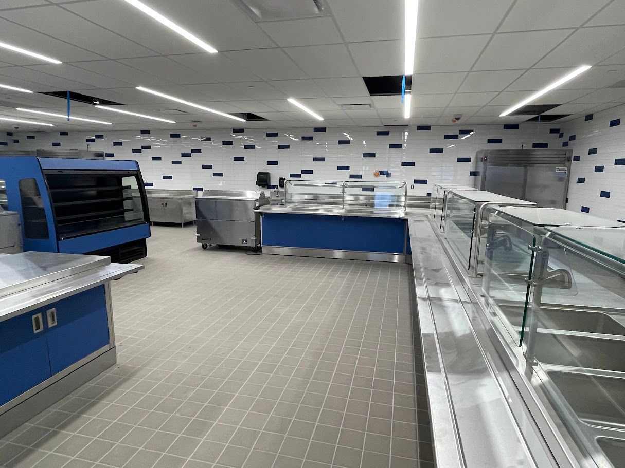 An empty commercial cafeteria or buffet line with blue counters, grey tiled floors, and white walls with blue accents.
