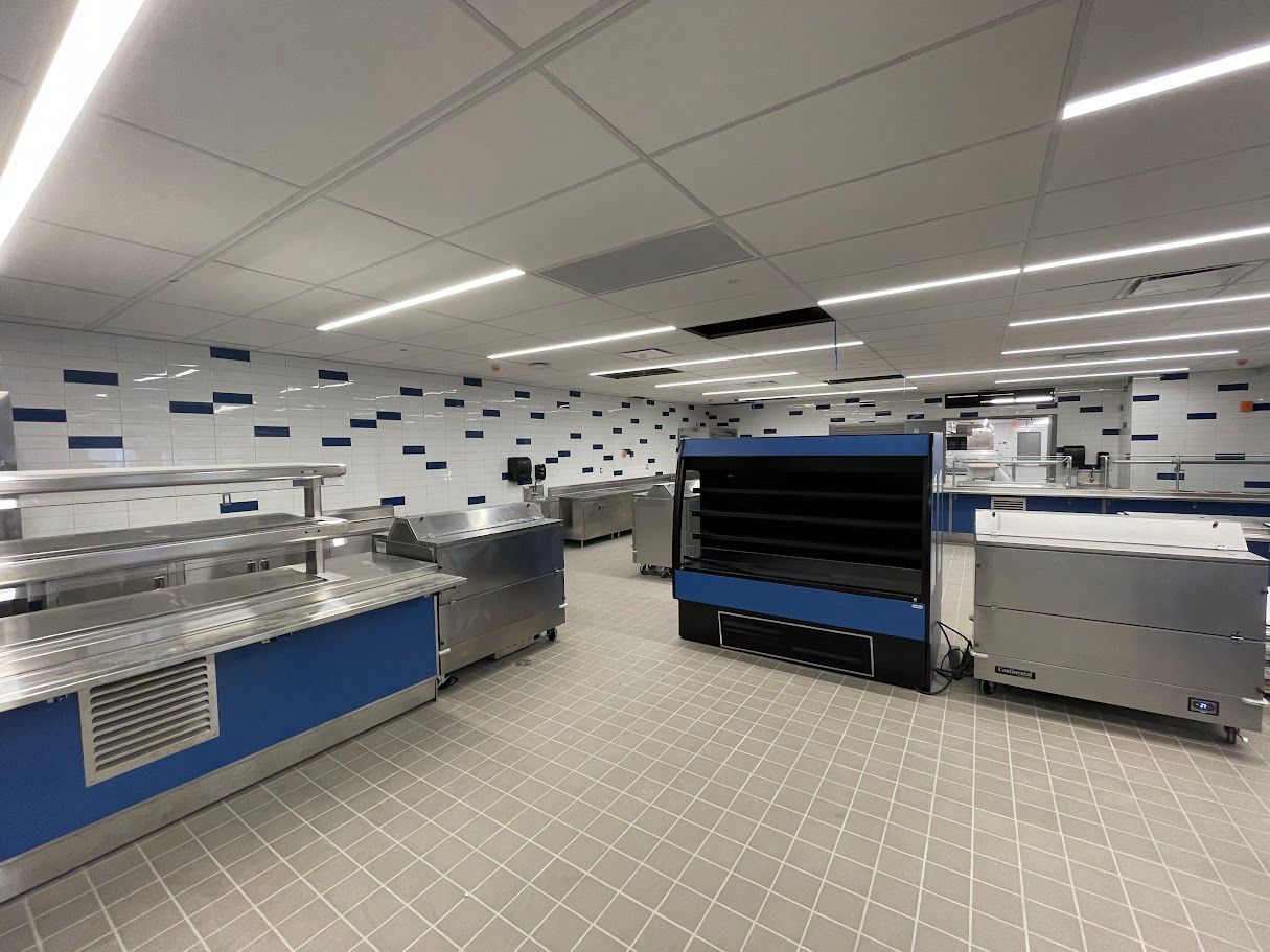 A modern cafeteria serving area with stainless steel counters, blue accents, and tiled flooring under bright lighting.
