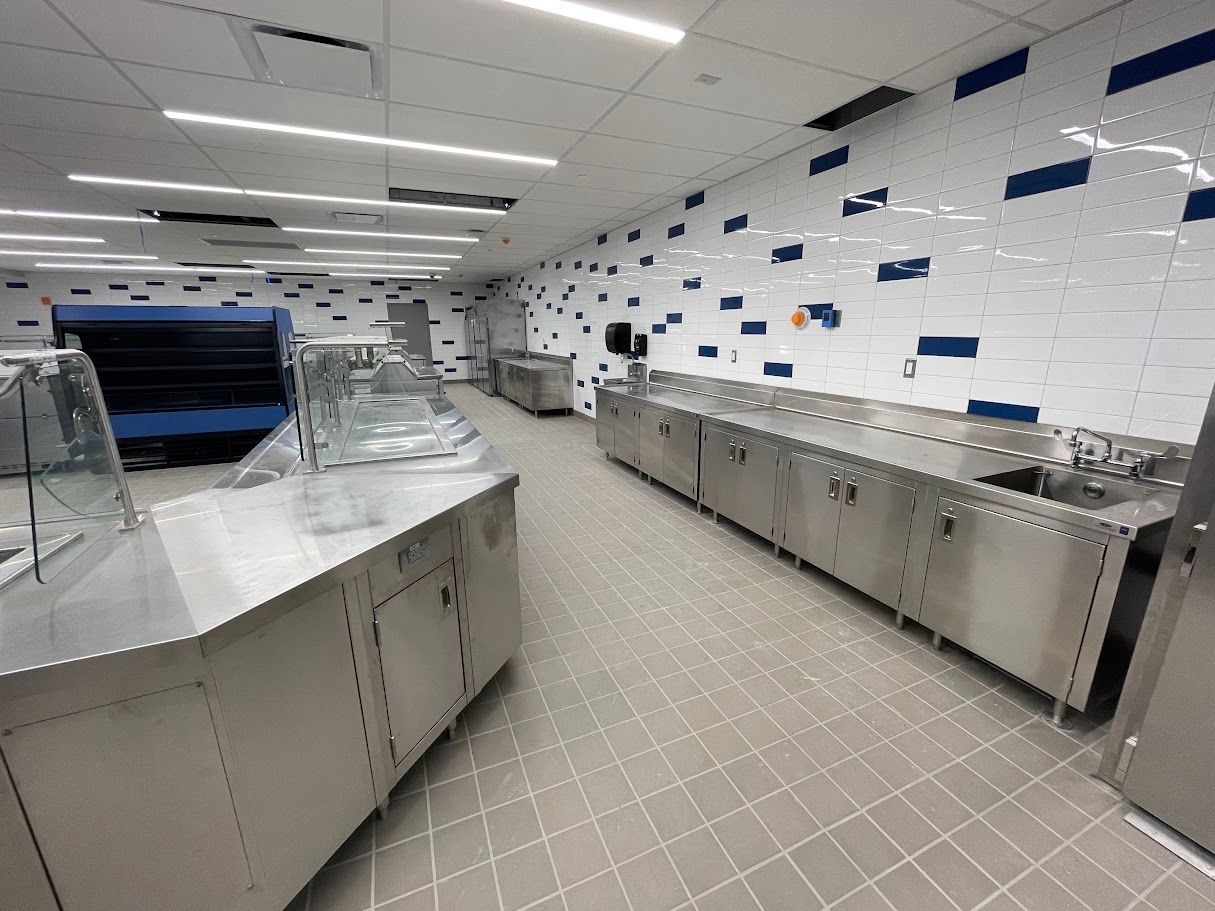 A modern commercial kitchen serving area with stainless steel counters and tiled walls featuring a blue-and-white pattern.