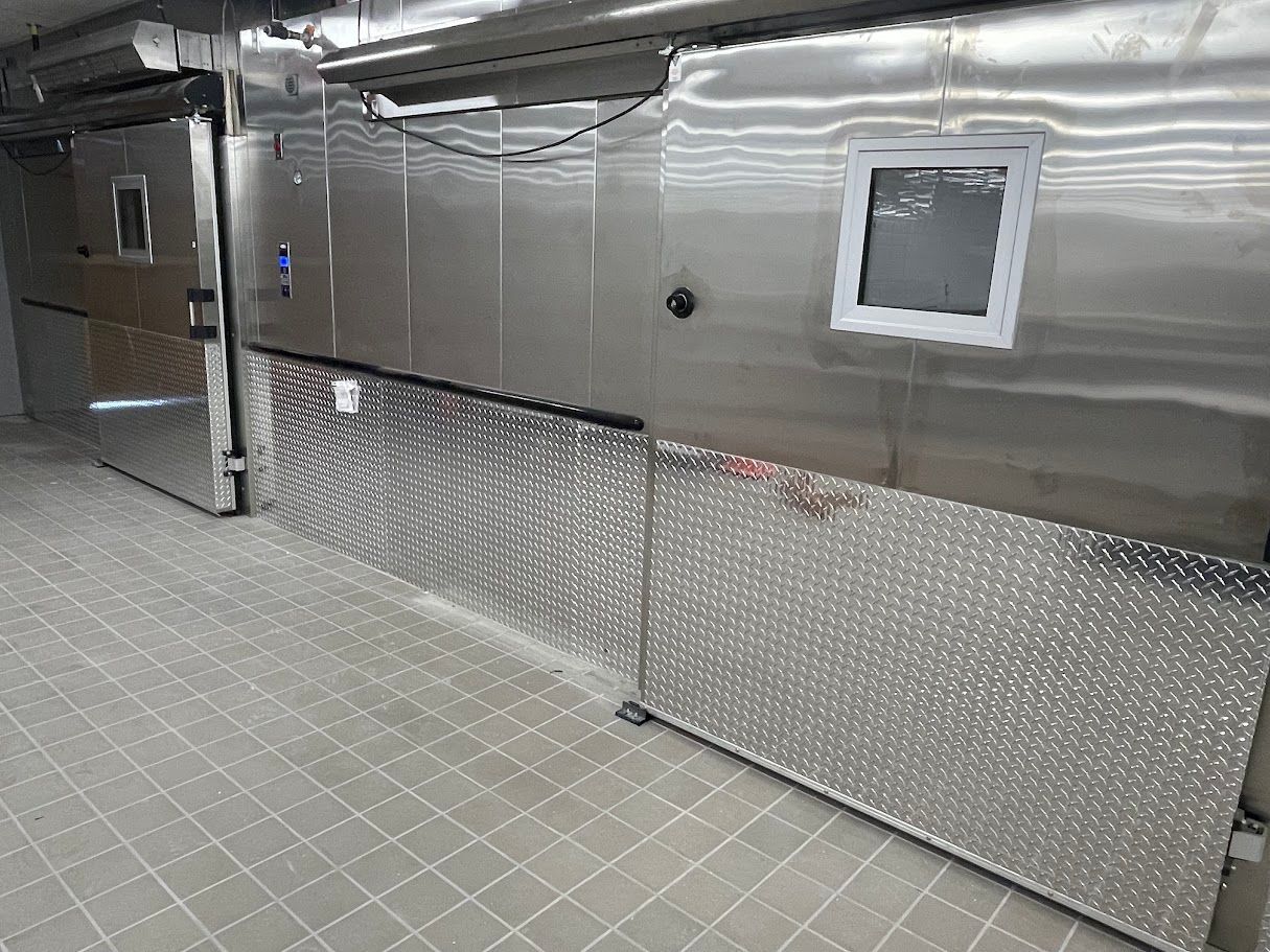 A commercial walk-in cooler or freezer with stainless steel walls and diamond-plate kick panels in a tiled room.