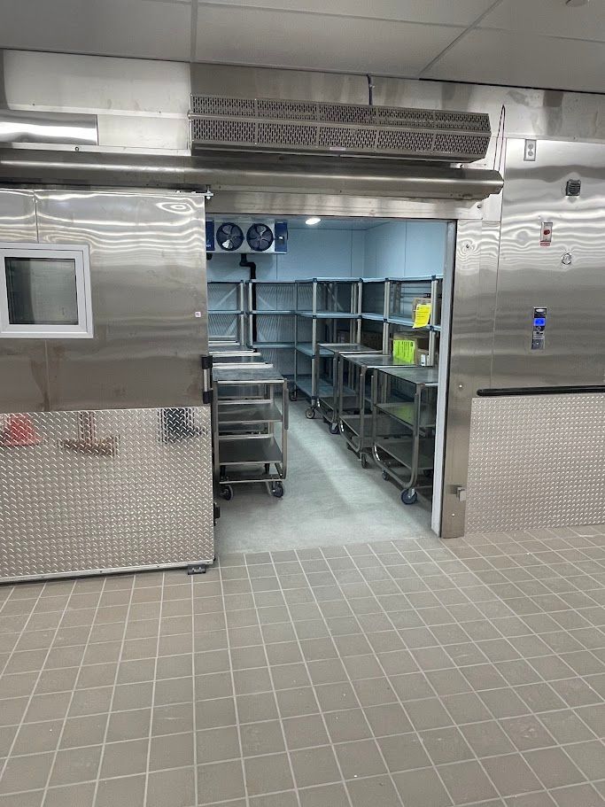 A stainless steel commercial walk-in freezer with metal shelving units on wheels inside a tiled kitchen.
