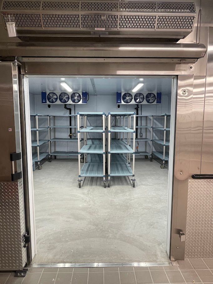 The interior of a commercial walk-in cooler featuring rows of metal shelving and ceiling-mounted refrigeration units.
