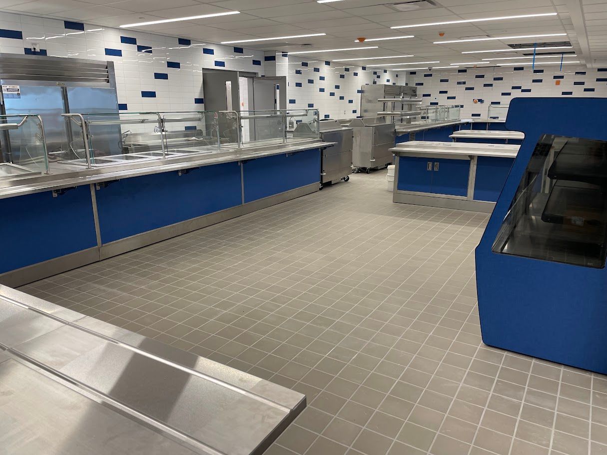 A clean, empty cafeteria serving area with stainless steel counters, blue bases, and light gray tiled floors.
