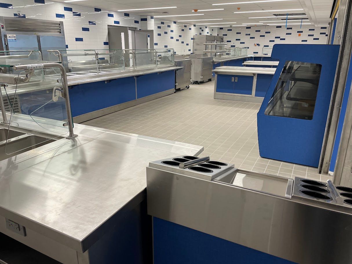 Empty cafeteria serving area with stainless steel counters and blue cabinets against a white, patterned wall.