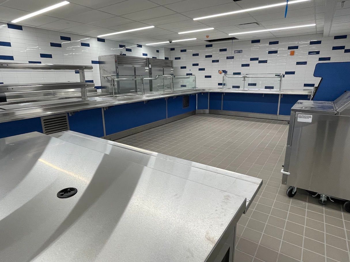 A clean, modern commercial kitchen with stainless steel counters, blue accents, and tiled walls and floors.