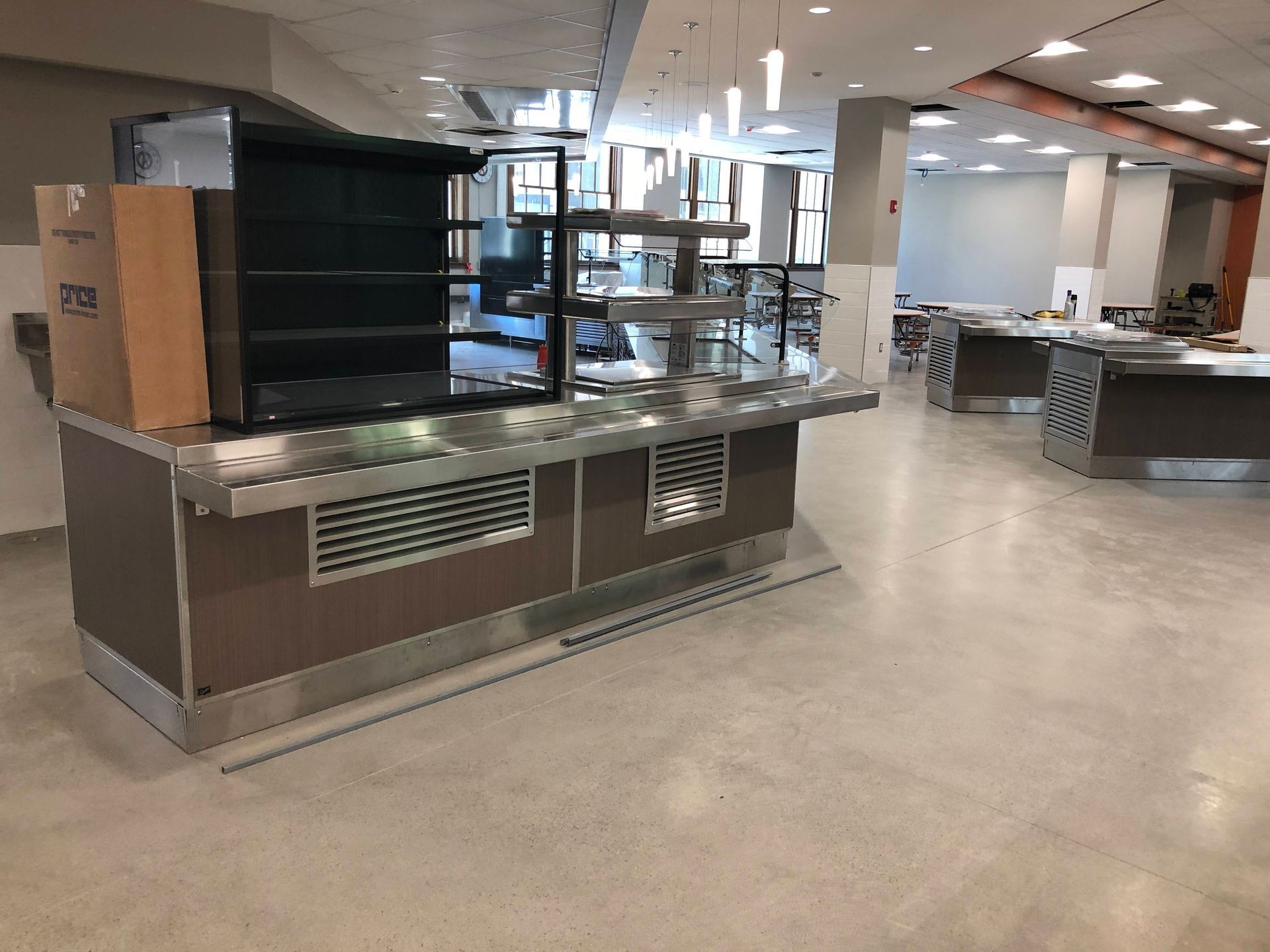 A stainless steel cafeteria serving station with shelving and a refrigerated display unit in a modern dining hall.