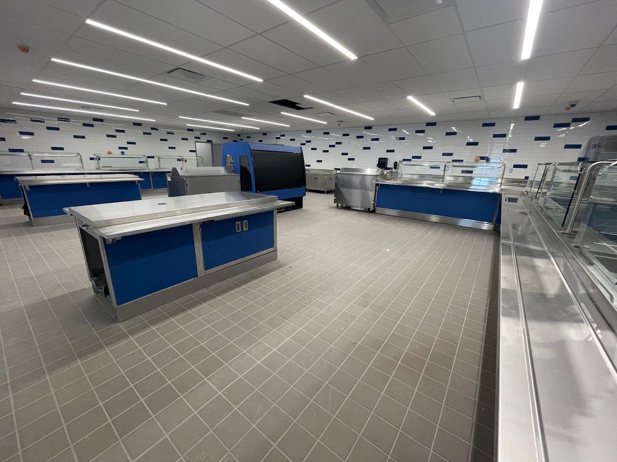 Modern cafeteria with blue service counters, white tiled floor, and linear LED lighting.