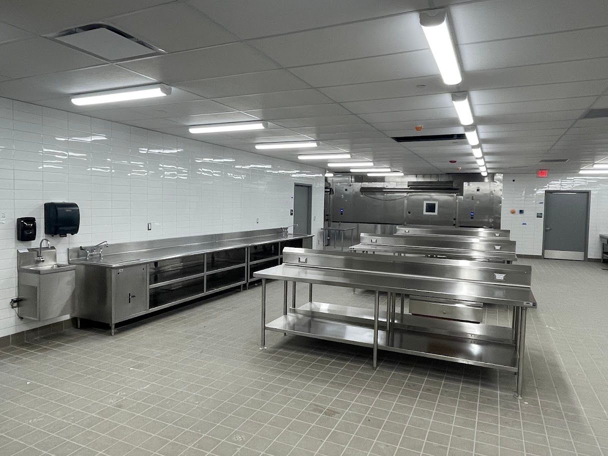 A sterile, commercial kitchen with stainless steel tables, white tiled walls, and bright overhead lighting.