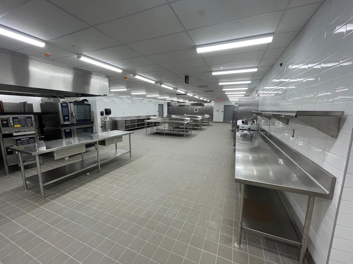 A wide-angle view of a clean, brightly lit commercial kitchen with stainless steel prep tables and appliances.