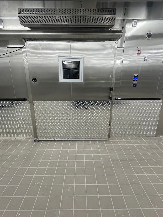 A stainless steel commercial walk-in freezer door with a small square window and diamond plate kick-plating.