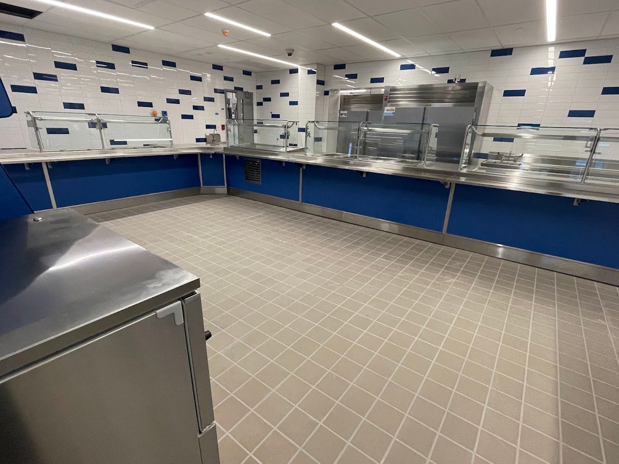 A clean, modern commercial kitchen serving area with stainless steel counters, blue paneling, and white tile walls.