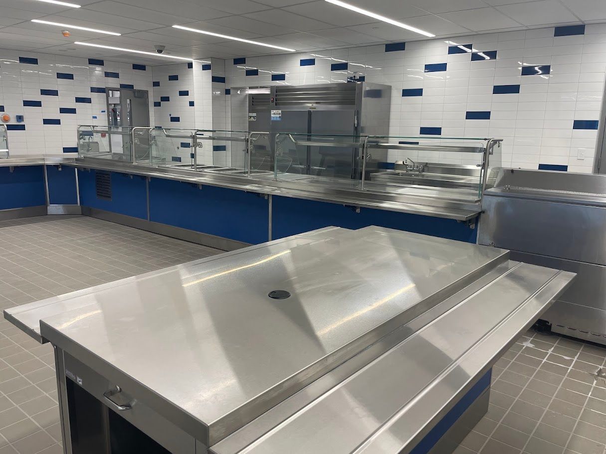 A stainless steel serving counter in a kitchen with blue cabinets, tiled walls, and reflective surfaces.