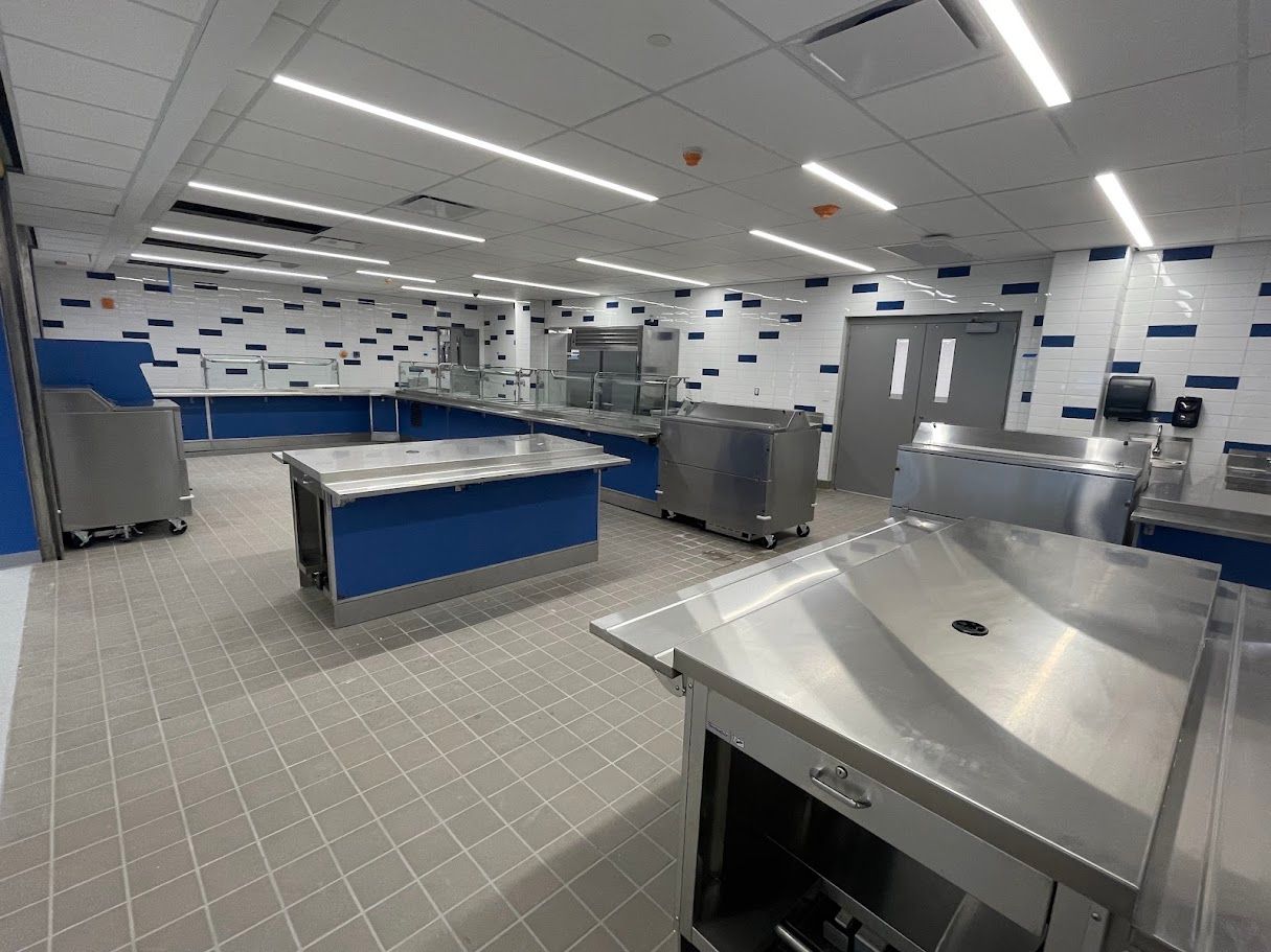 A modern commercial kitchen serving area with stainless steel counters, blue accents, and tiled walls and floors.