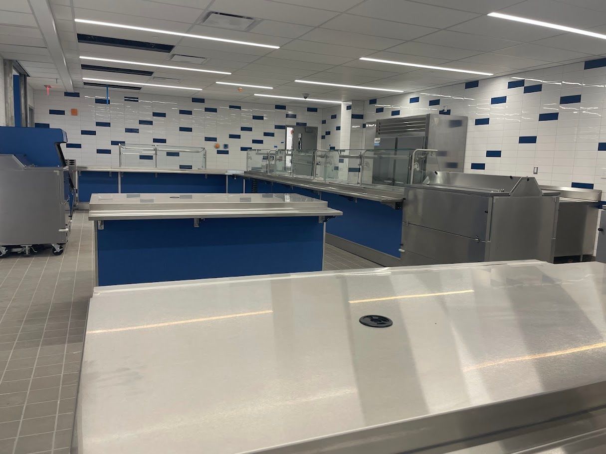 A bright, modern cafeteria serving area with stainless steel counters and blue accent panels against a tiled wall.