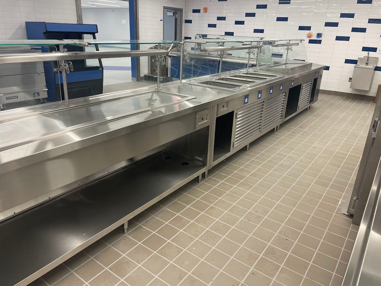 A stainless steel cafeteria serving line with tiled floors and blue accent walls.
