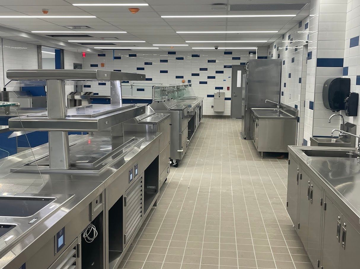 A clean, commercial kitchen with stainless steel countertops, prep stations, and white tile walls with blue accents.