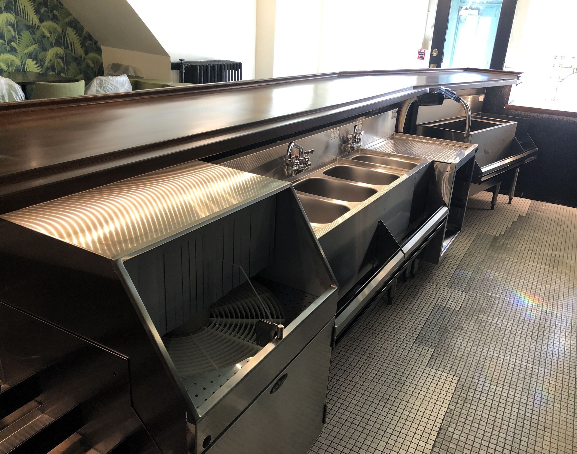 A stainless steel bar sink unit with three compartments and a glass rinser in a clean, commercial interior.