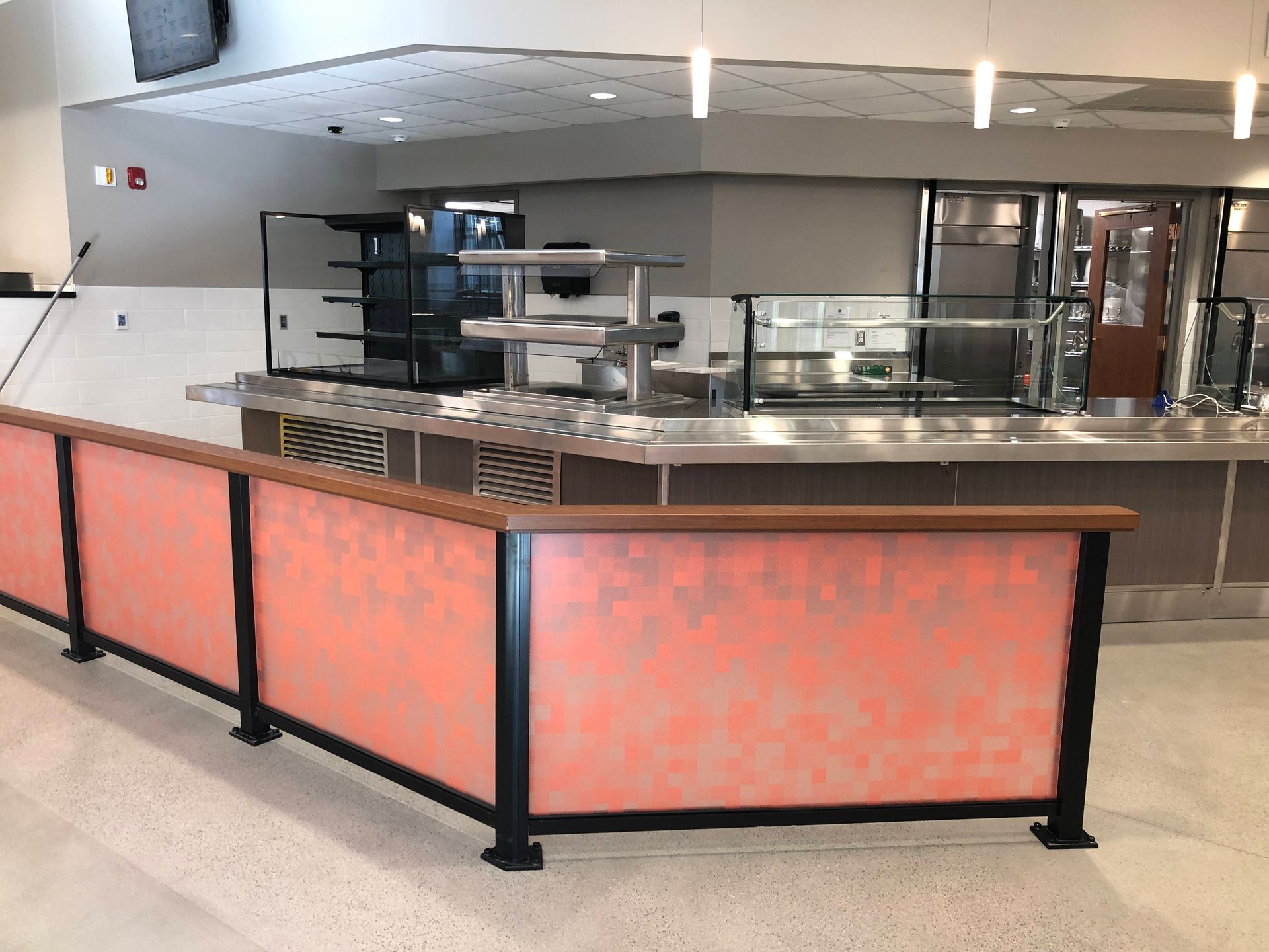 A cafeteria service counter featuring a salmon-colored partitioned barrier in front of stainless steel food stations.