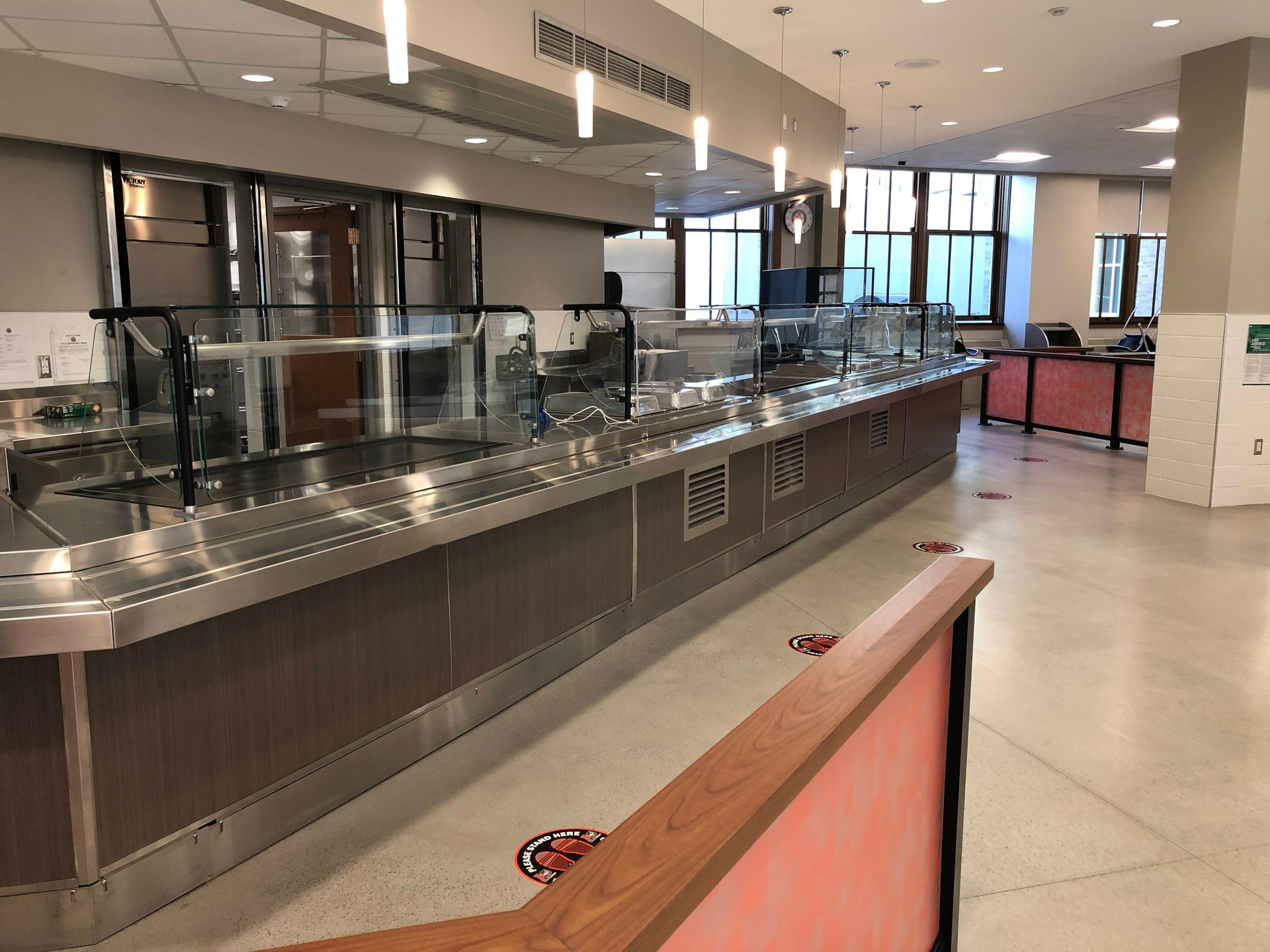 A clean, empty cafeteria buffet serving area with stainless steel counters and light-colored floors.