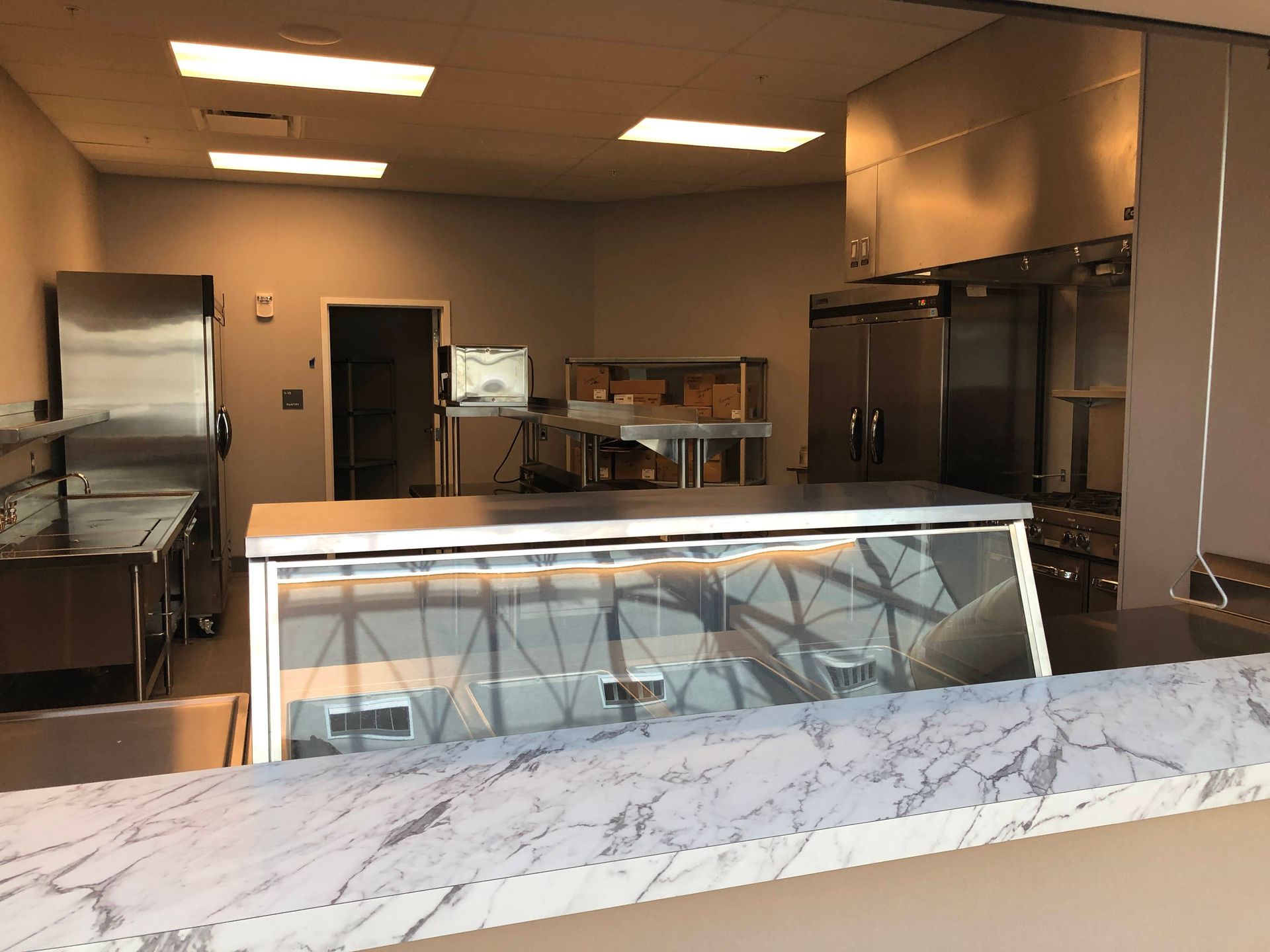 A professional kitchen with a marble-topped service counter, stainless steel appliances, and a glass display case.