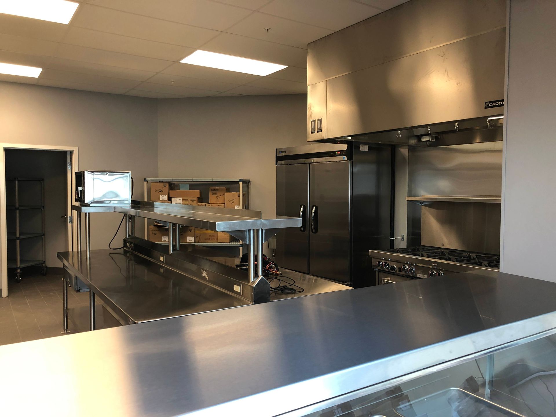 A commercial kitchen featuring stainless steel counters, a refrigerator, and a stove under a large ventilation hood.