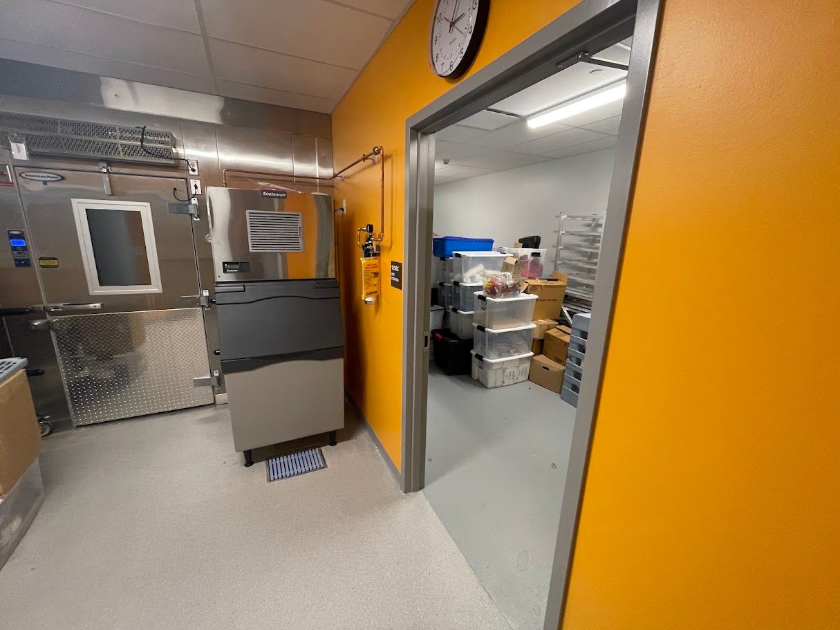 A grey appliance stands in a room with orange walls and a doorway leading to a storage room with stacked plastic bins.
