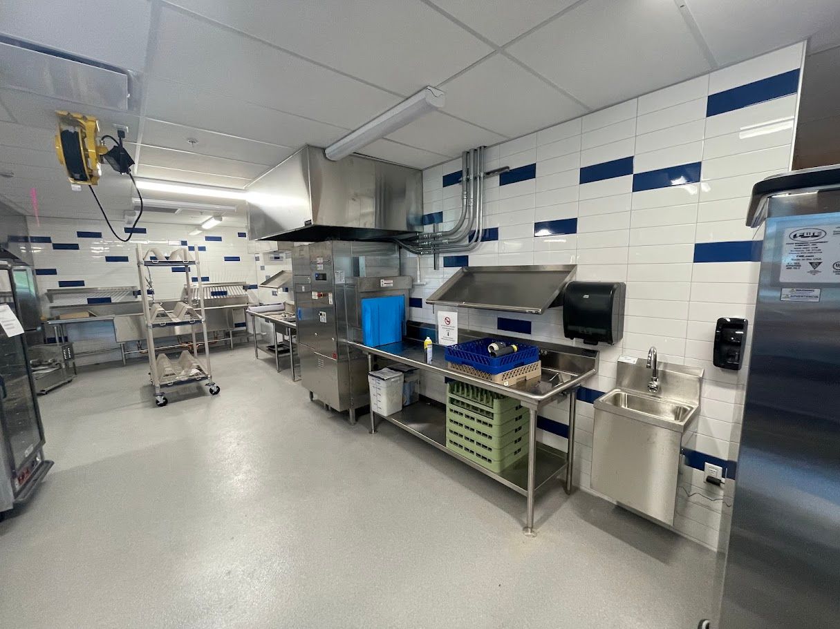 A modern industrial kitchen with stainless steel equipment, tiled walls with blue accents, and a food preparation counter.