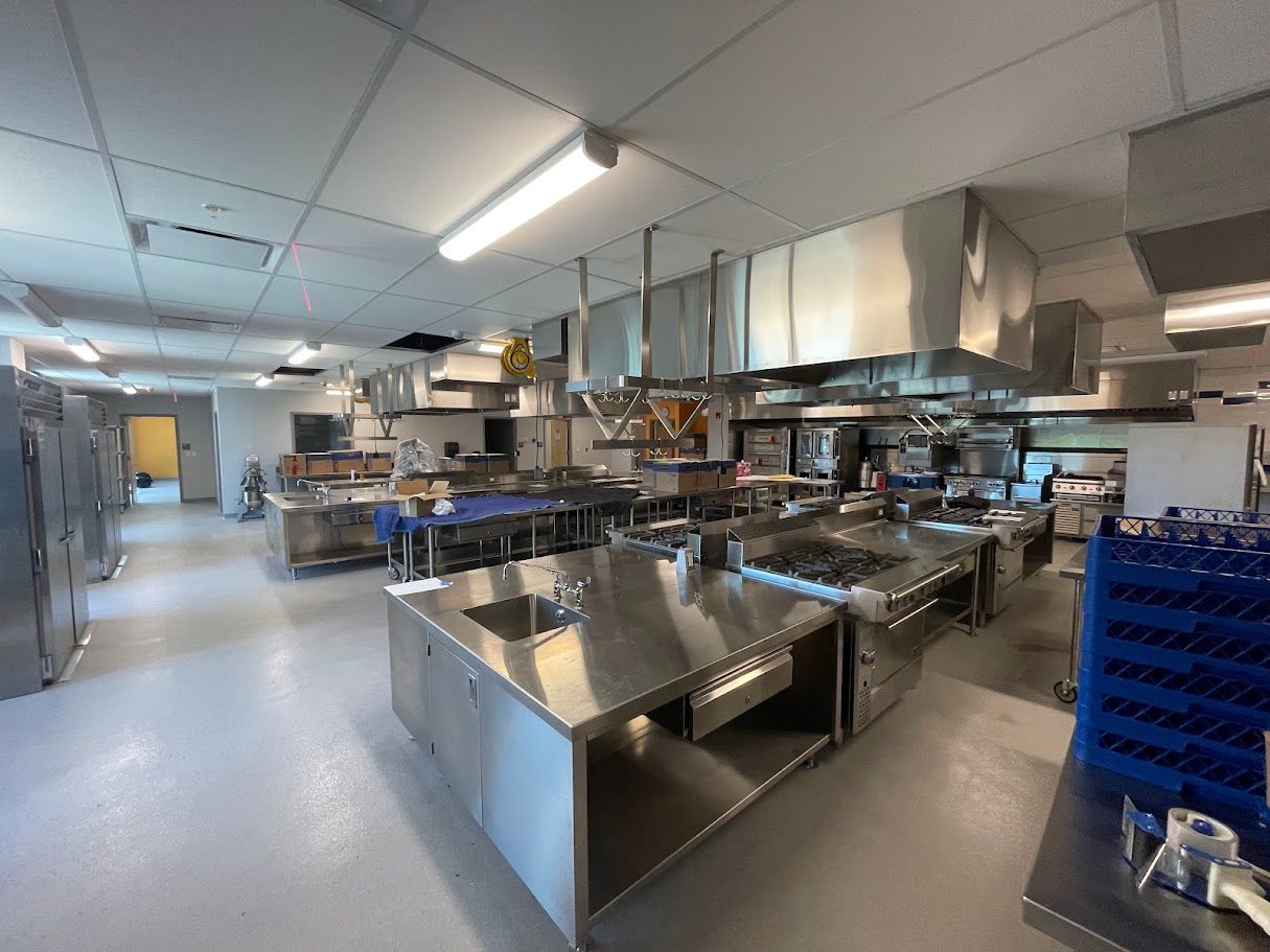 A professional industrial kitchen with stainless steel work tables, cooking ranges, hoods, and blue storage crates.