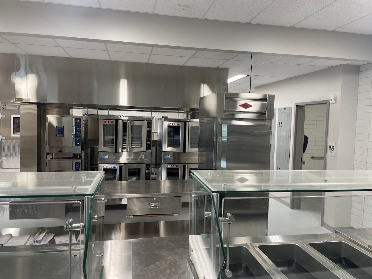 Commercial kitchen interior featuring stainless steel ovens, refrigerators, and glass service counters.