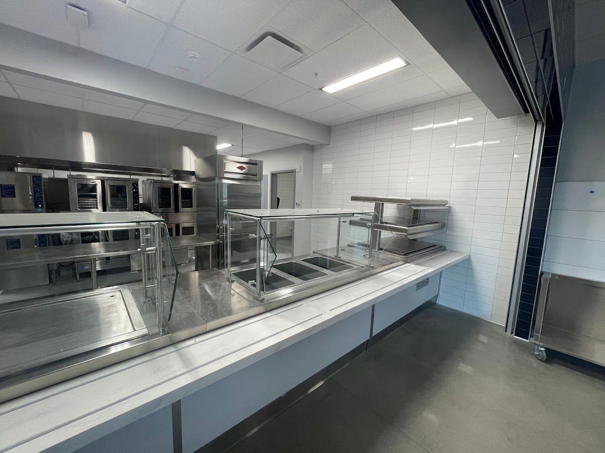 A stainless steel commercial kitchen serving line with food warmers and white subway tile walls.