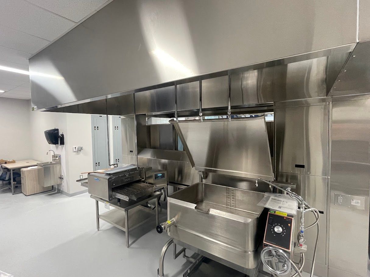 A stainless steel commercial kitchen hood installed above a tilting skillet and countertop cooking equipment.