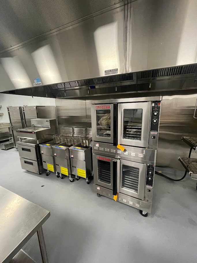 A commercial kitchen featuring a stainless steel double-stacked oven and a line of fryers under a large exhaust hood.