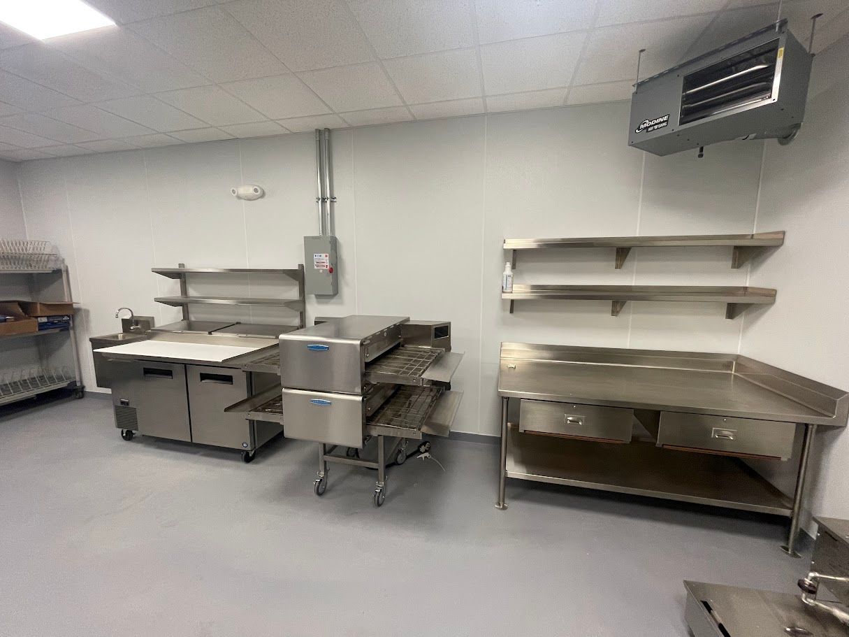 A commercial kitchen with stainless steel tables, shelving, and a heater mounted on the ceiling.