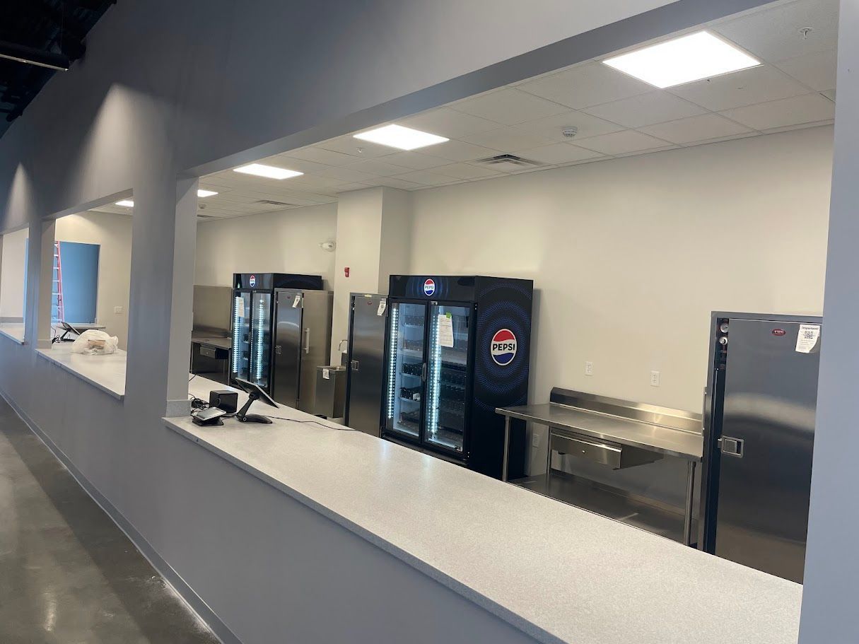 A concession stand featuring a long white counter, stainless steel food prep surfaces, and two glass-front refrigerators.