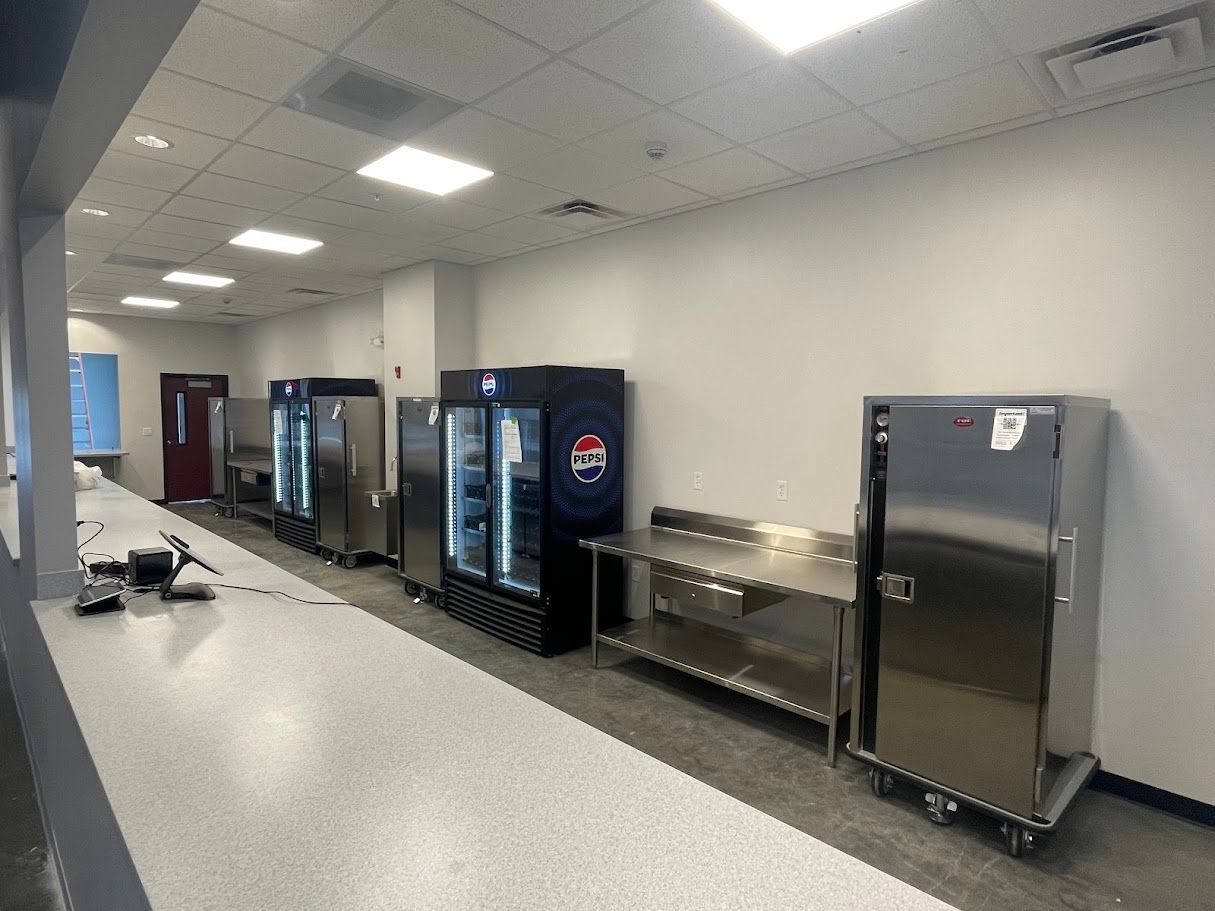 A commercial kitchen area featuring stainless steel prep tables, a display refrigerator, and a tall metal warming cabinet.