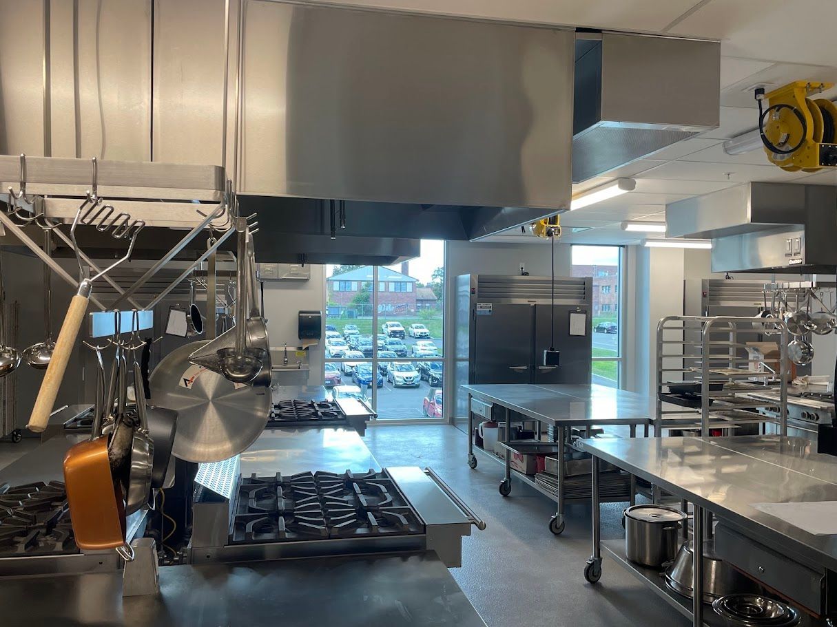 A commercial kitchen featuring stainless steel stoves, hanging cookware, a food slicer, and rolling prep tables.