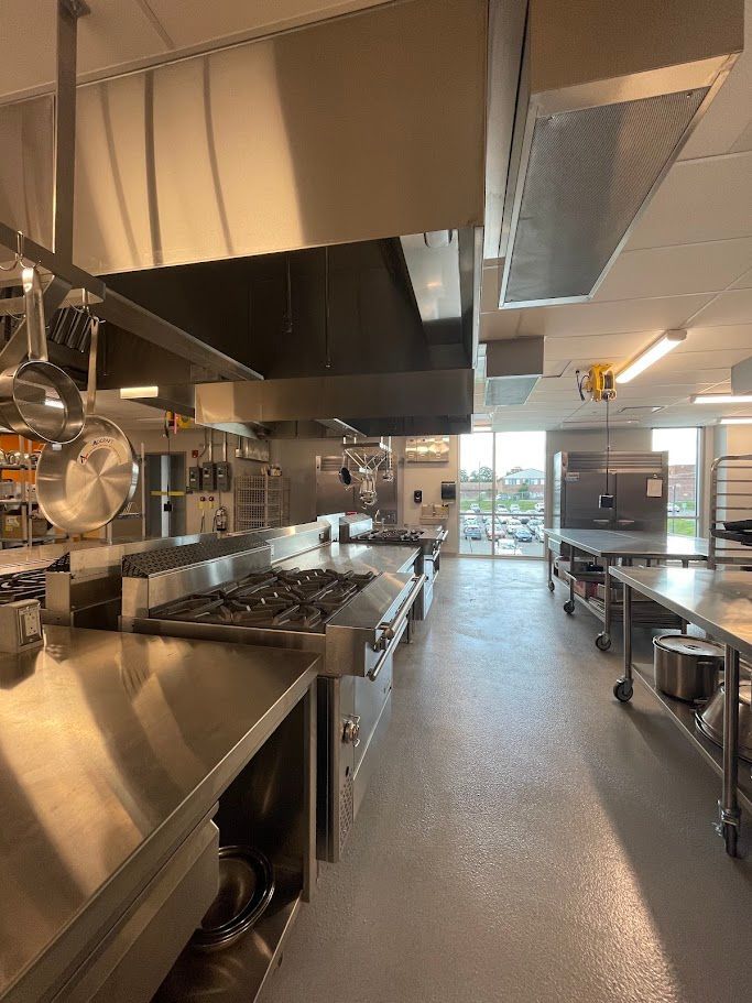 A wide shot of a commercial kitchen featuring stainless steel counters, a gas range, and overhead ventilation hoods.