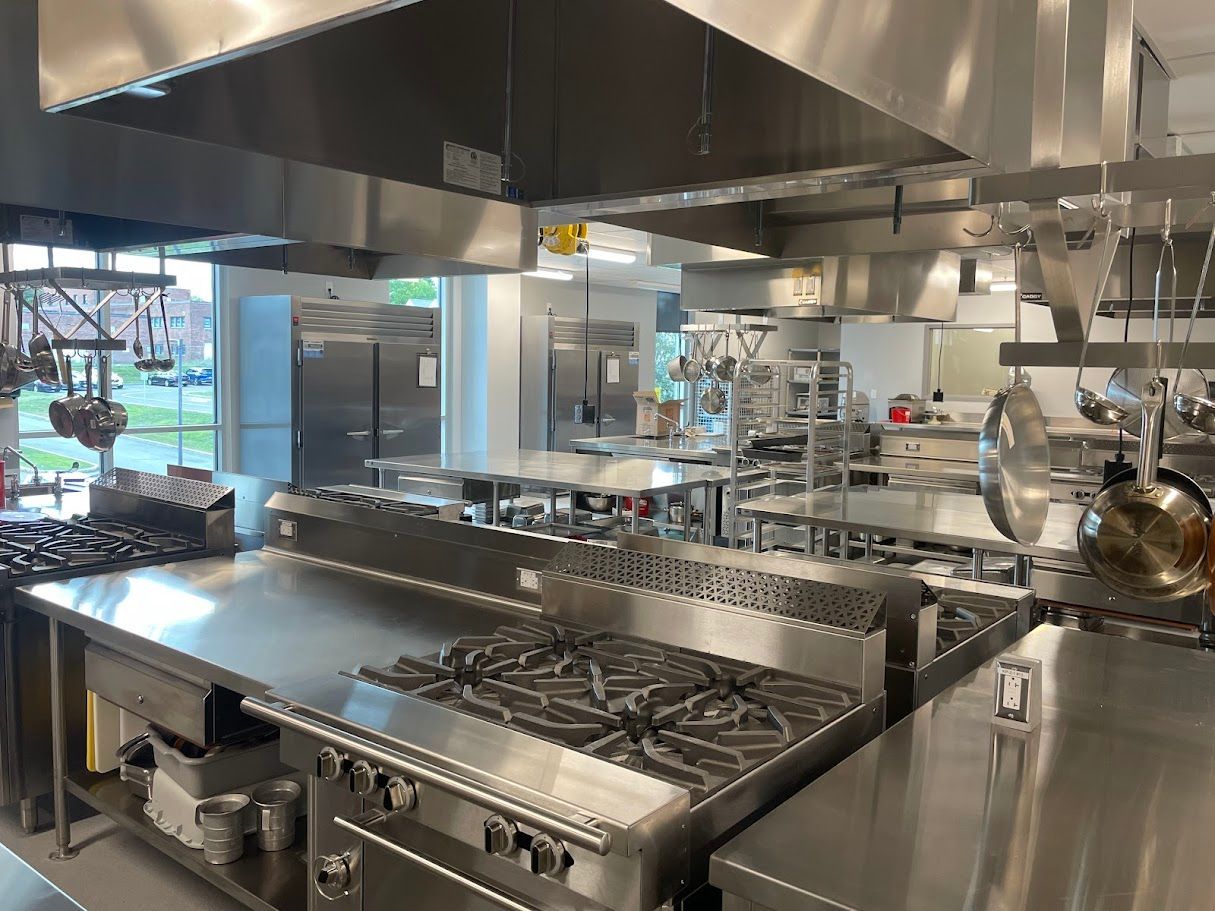 A commercial kitchen featuring stainless steel stoves, work counters, and hanging cookware under large ventilation hoods.