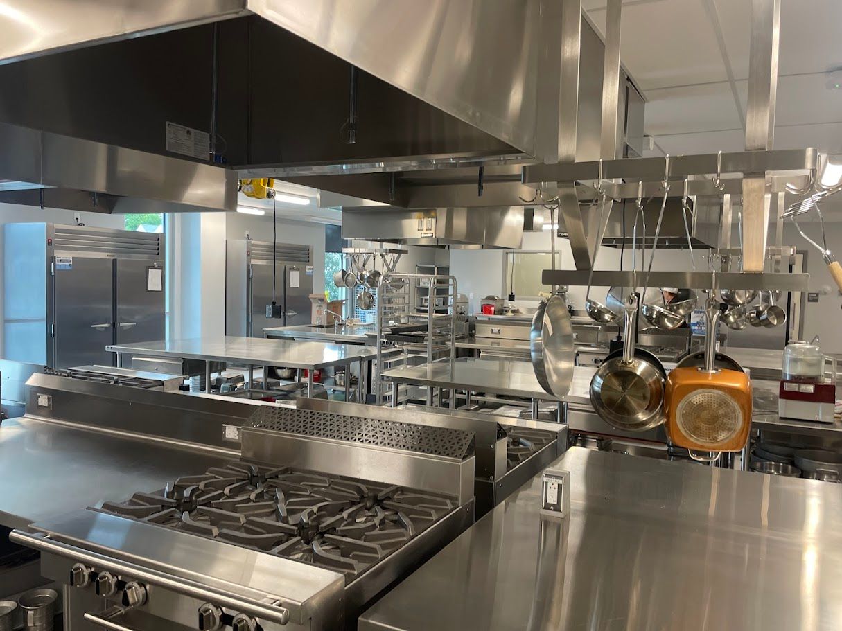 Professional commercial kitchen with stainless steel stoves, hanging cookware, and large refrigerators.